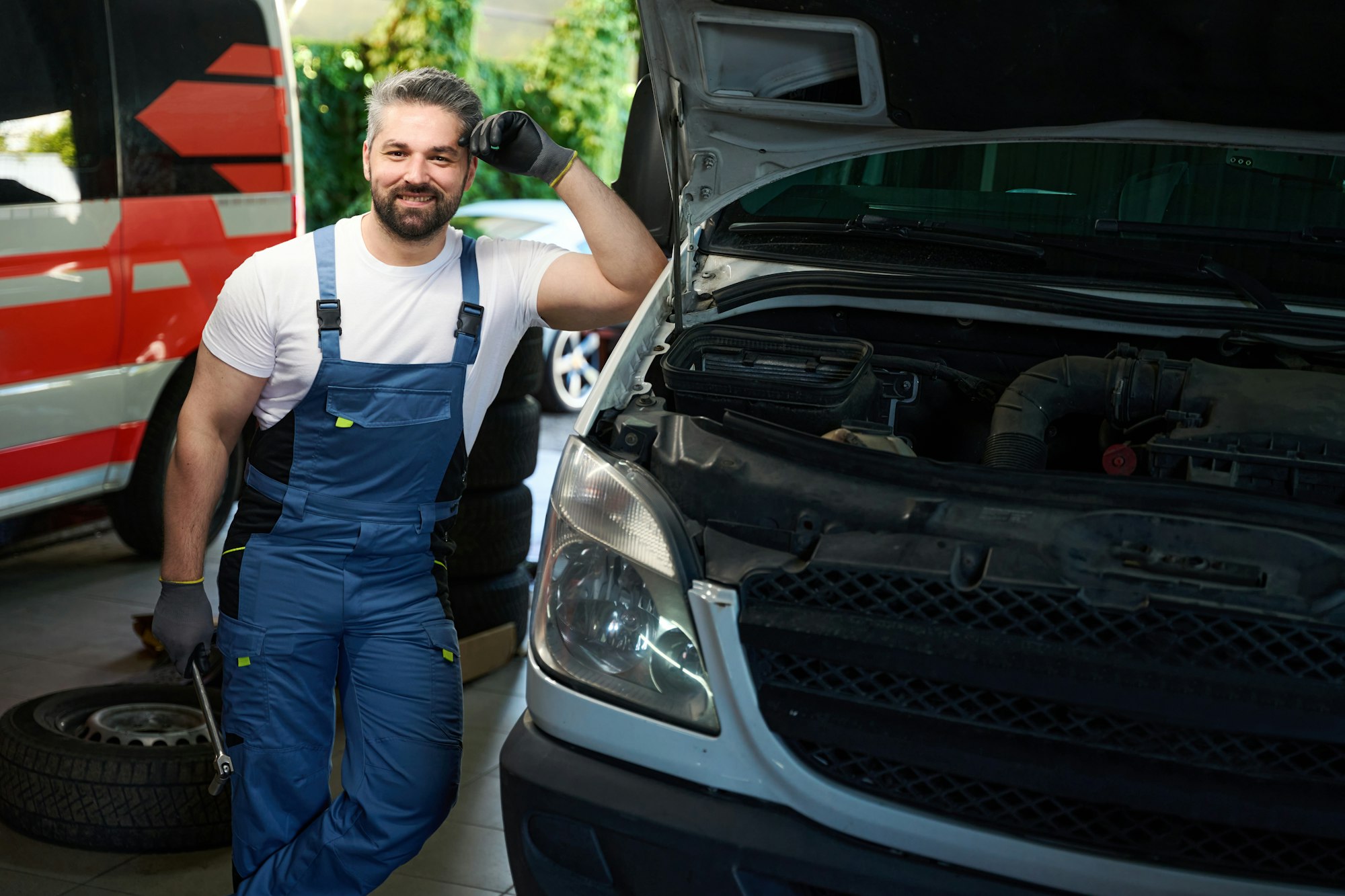 Smiling car service station worker posing for camera beside van